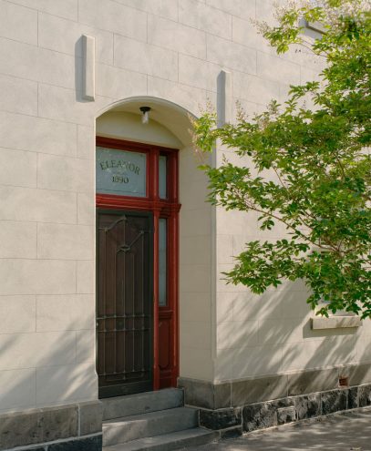 Elegant building entrance with a black door and red frame, surrounded by a white wall and greenery.