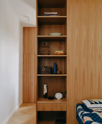 Modern wooden bookshelf with decorative items in a minimalist room.